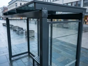 Robuste Bushaltestelle aus Stahl und Hartglas mit anthrazitfarbenem Aluminiumrahmen und antigraffiti-Beschichtung auf städtischem Platz.